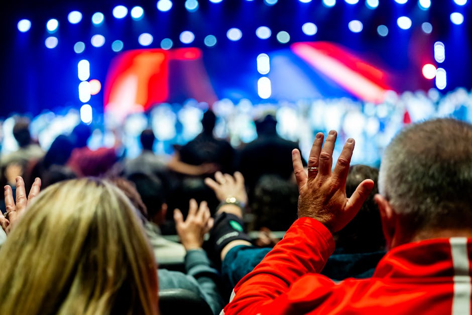 A lively audience raising hands at a colorful live concert with bright stage lights.