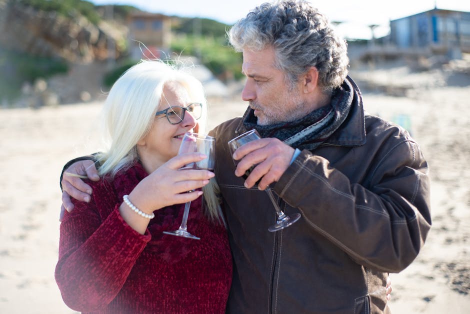 Happy senior couple sharing wine on a sandy beach in Portugal.