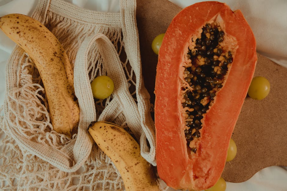Close-up of sliced papaya and bananas in a net bag surrounded by grapes, showcasing fresh tropical fruits.