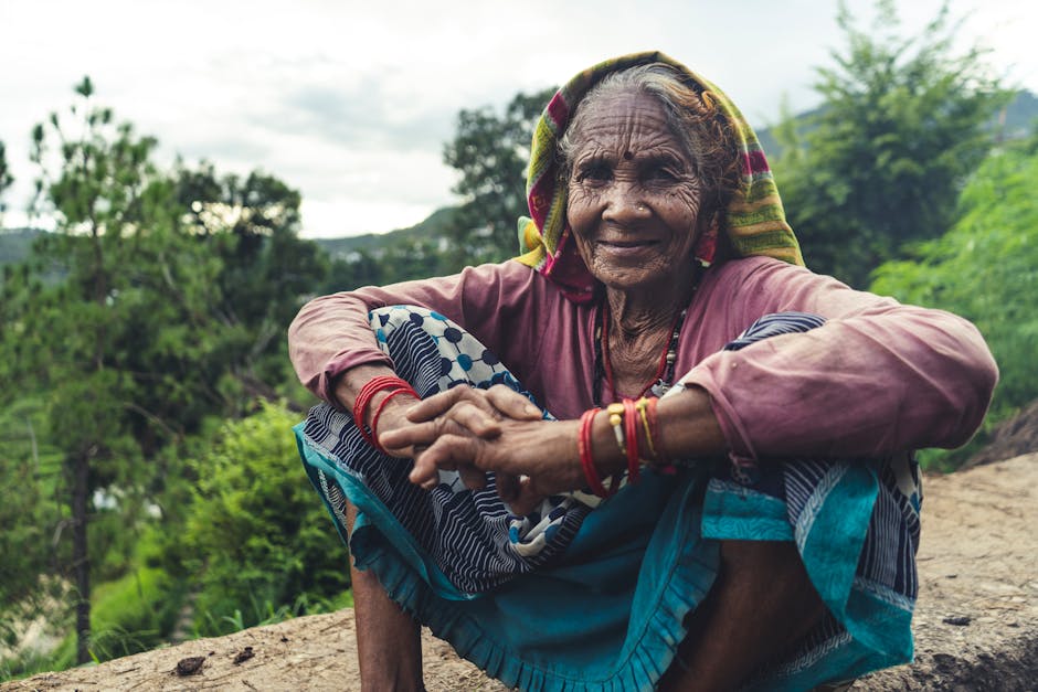 Smiling elderly Indian woman in traditional attire sitting outdoors in nature.