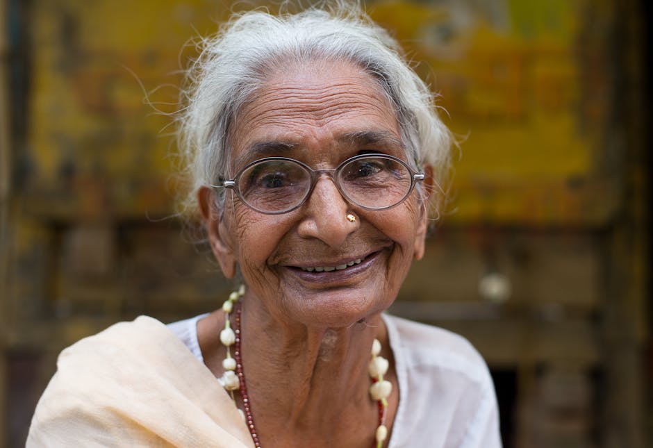 A joyful elderly woman with glasses smiling warmly in an outdoor setting.