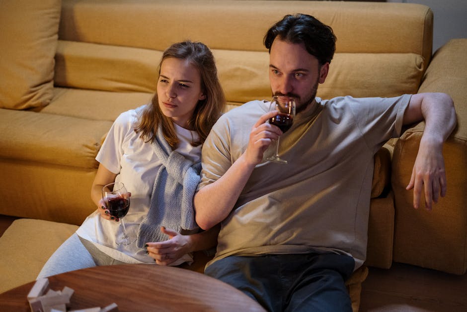 A couple sitting on a sofa at home, enjoying glasses of wine in a cozy setting.