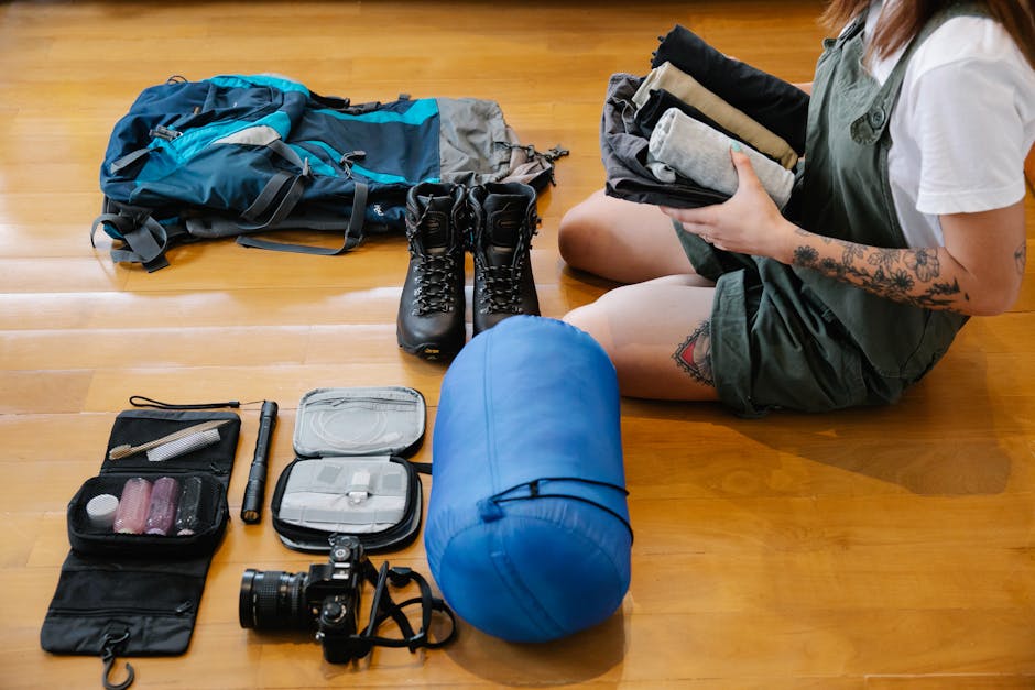Woman organizing camping gear and clothes on wooden floor indoors, preparing for an adventure.