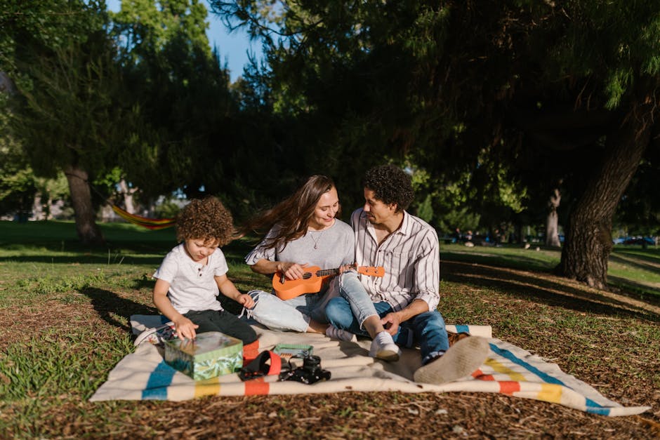 A joyful family enjoying a summer picnic with a ukulele in a sunny park setting.
