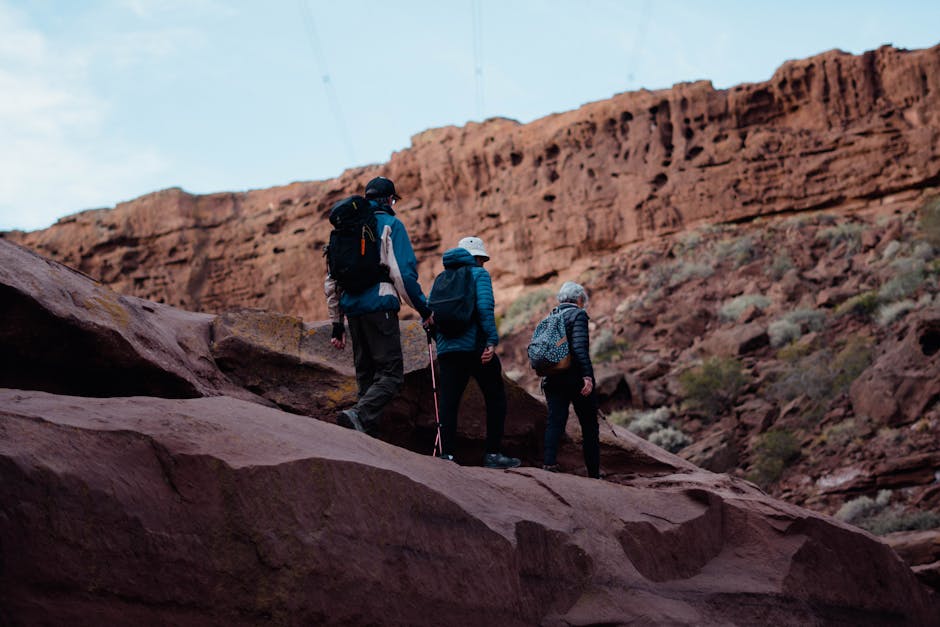 Three hikers traversing rocky terrain in a red rock canyon, showcasing adventure and exploration.