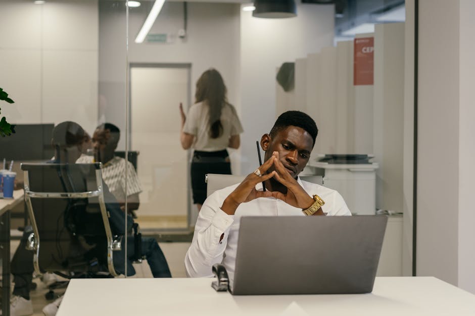 African American man concentrating at his laptop in a contemporary office environment with coworkers.