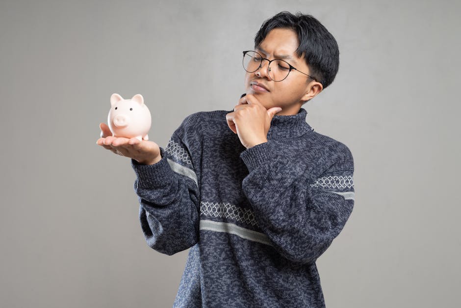 Young adult in glasses holding a piggy bank, pondering savings indoors.