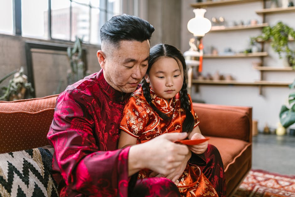 Father and daughter in tang suits holding a red envelope in a festive living room.