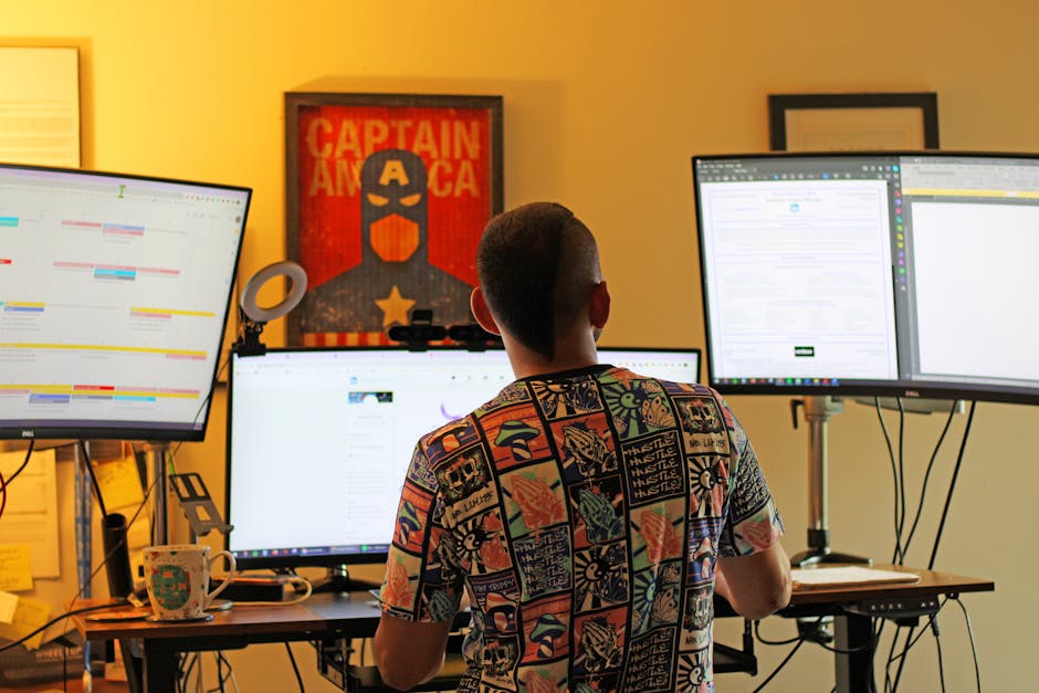 Man working from home office with multi-monitor setup, back view.