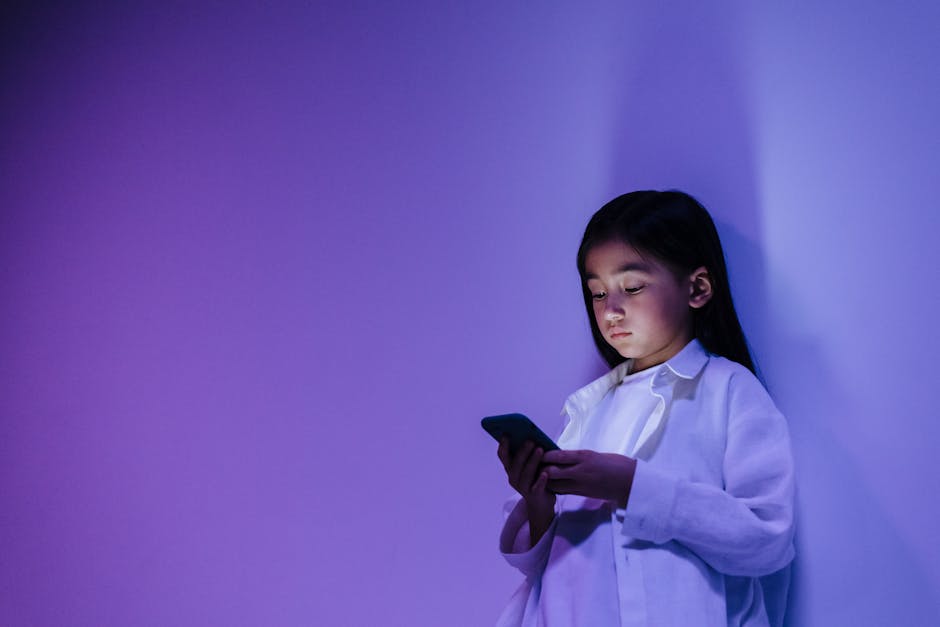 Young girl engrossed in smartphone against a vibrant purple wall indoors.