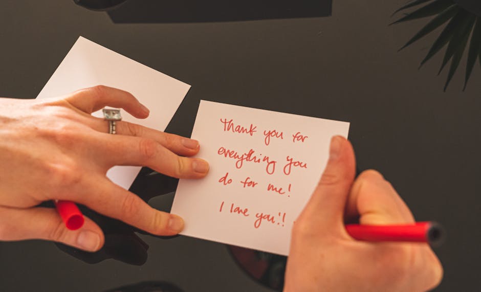 A person writing a heartfelt thank you note with a red pen on white paper.