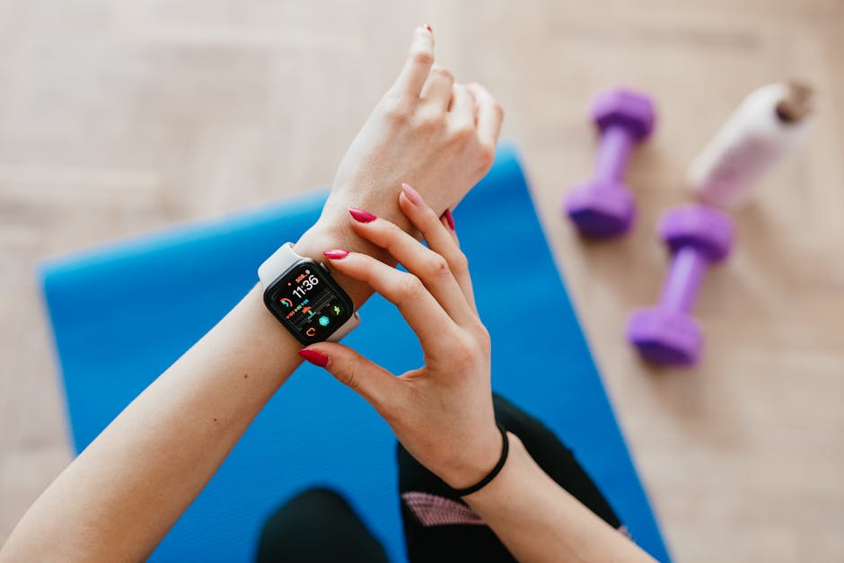 Unrecognizable female in sportswear sitting on blue yoga mat on floor and checking smart watch