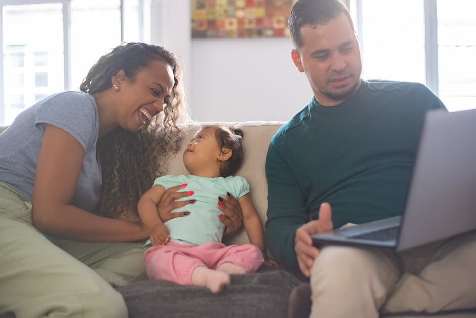 A joyful family moment on the sofa with parents and a toddler playing and using a laptop.