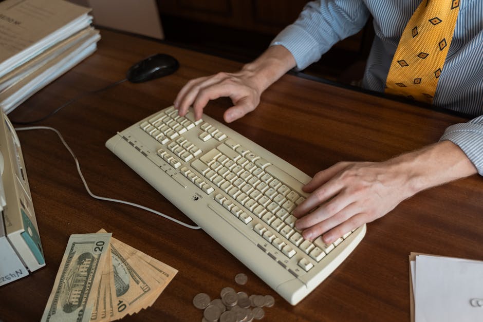 Hands typing on a vintage keyboard on a wooden desk with cash and coins.
