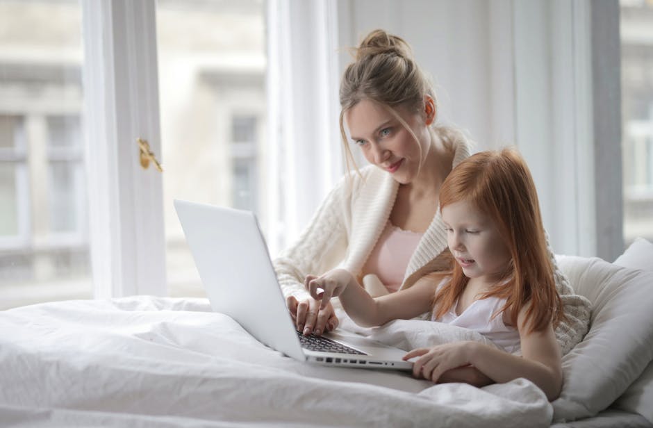 A mother and daughter bonding and enjoying laptop time together in bed, indoors.