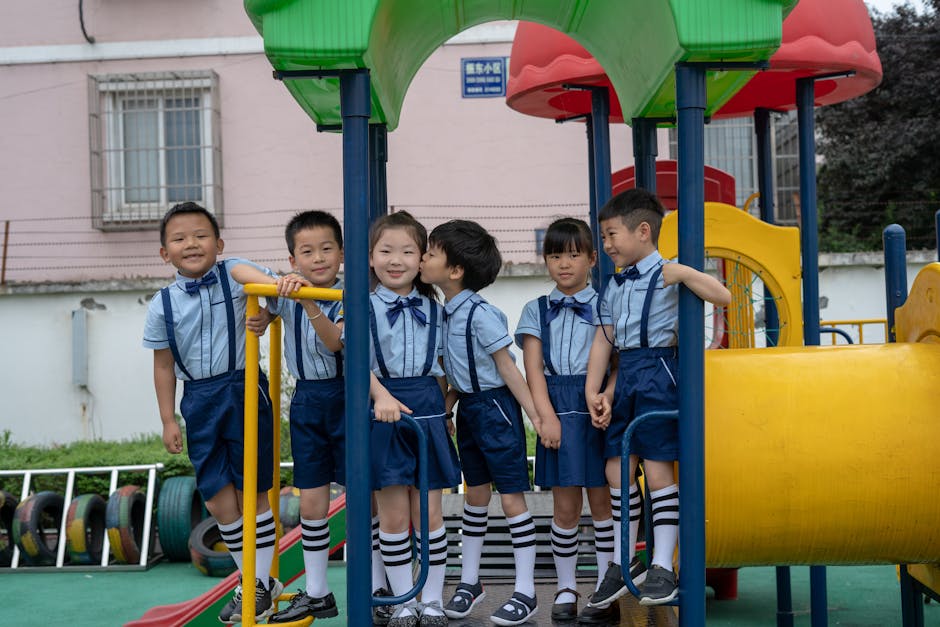 Children in formal school uniforms playing on colorful playground equipment outdoors.