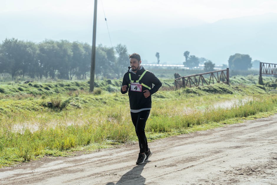 Adult male runner in a black outfit jogging on a rural trail during daylight.
