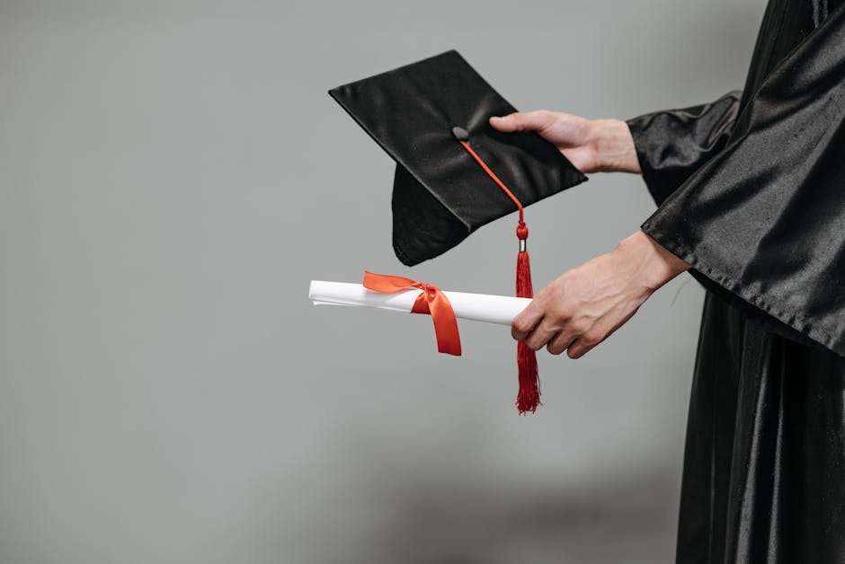 Close-up of graduate holding cap and diploma with red ribbon, symbolizing success.