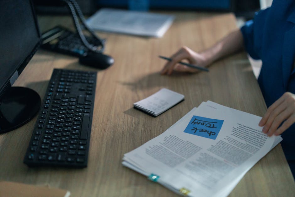A close-up of a computer keyboard and documents on a desk in an office setting, highlighting workplace organization.