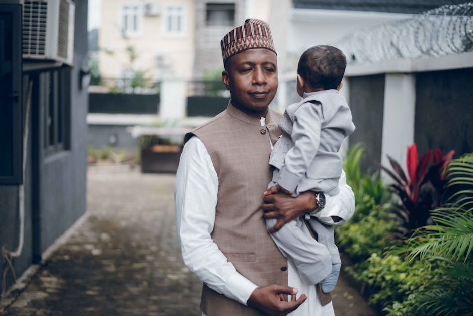 A man in traditional clothing holds a baby outdoors, conveying warmth and family connection.