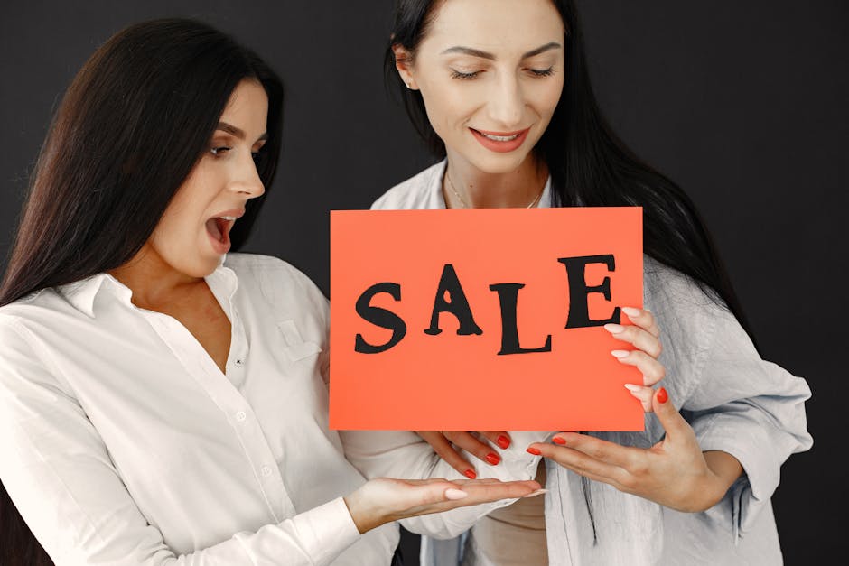 Two women energetically holding a 'SALE' sign, showcasing excitement and enthusiasm for a shopping event.