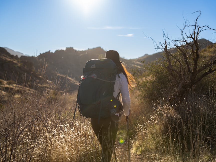 Backpack-wearing woman hikes through Superstition Mountains, AZ under the morning sun.