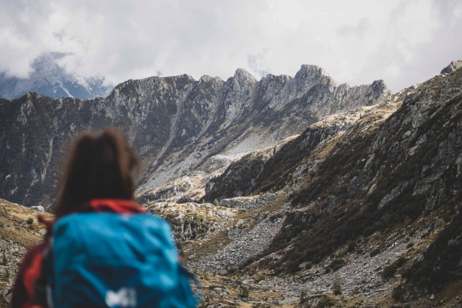 A woman hiking with a backpack in a stunning mountain range with rocky terrain.