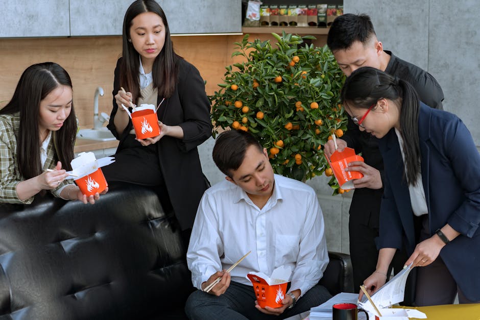 Office team enjoys a casual lunch break indoors, eating Asian noodles and discussing ideas.