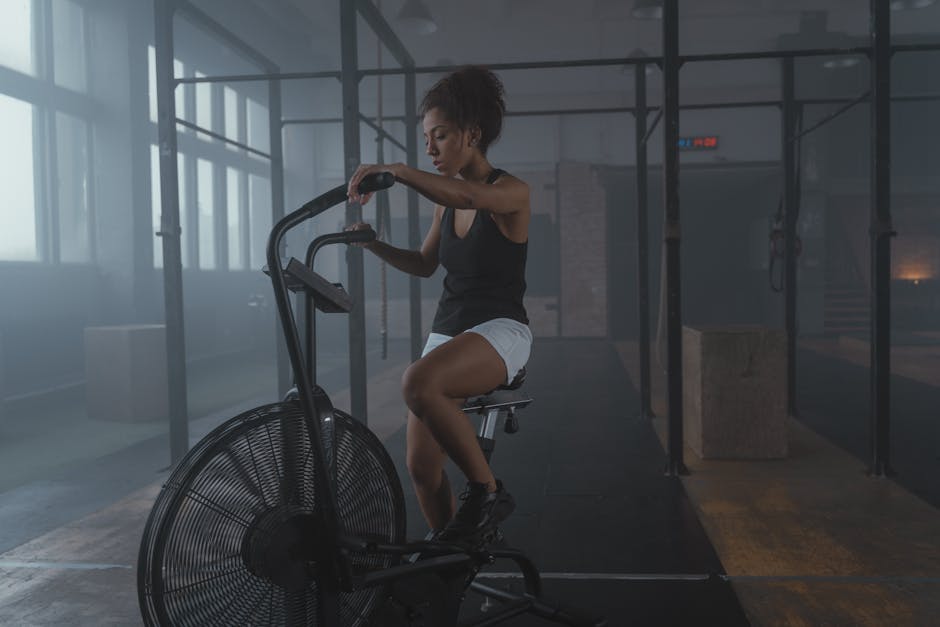 African American woman exercising on an air bike in a gym, showcasing fitness and strength.