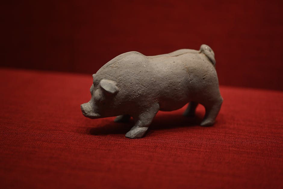 A rustic clay pig figurine placed on a vibrant red textile background.