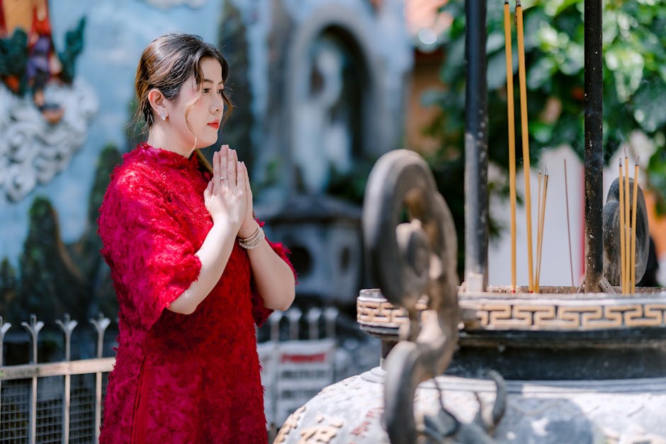 A woman in a red dress praying by incense at a shrine outdoors.