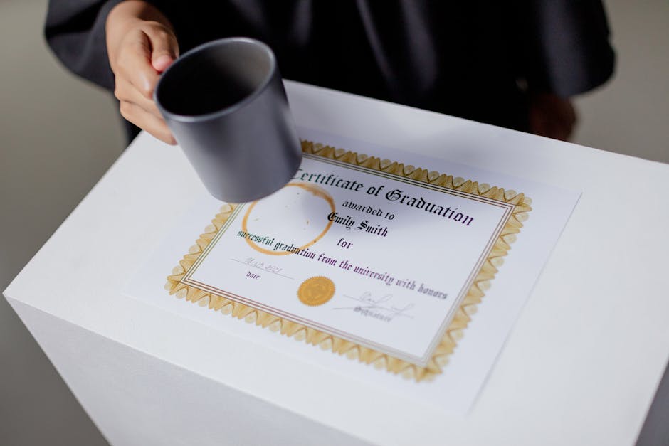 A graduation certificate on a white table with a hand holding a mug, symbolizing achievement.