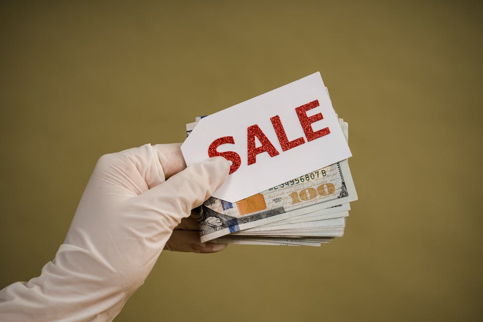 A hand wearing latex gloves holds a stack of dollar bills with a sale sign, symbolizing discount or cash transaction.