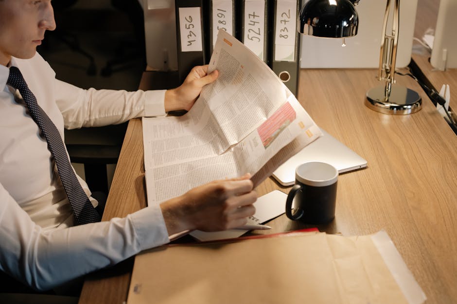 A focused businessman reads a newspaper at a wooden desk in his office, emphasizing work and information.