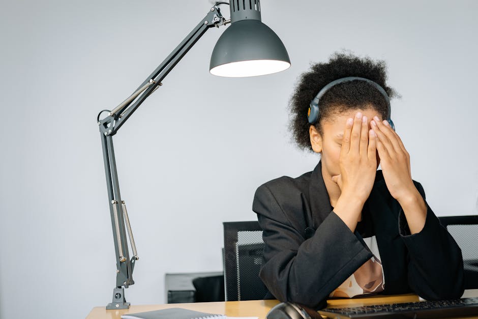 Overworked call center agent with hands on face, feeling exhausted while working in the office.