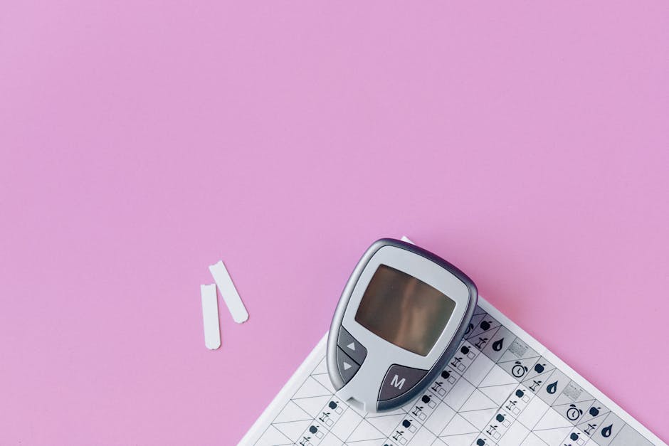 Flat lay of a blood glucose monitor and test strips on a pink surface.