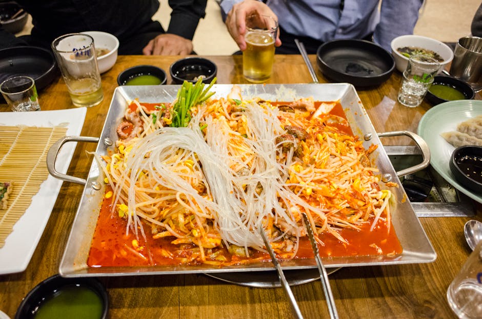 A vibrant tabletop spread featuring spicy Korean hot pot with rice noodles and various side dishes.
