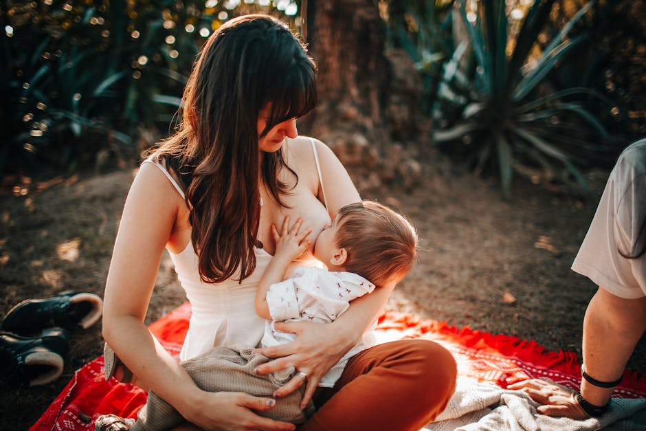 Woman breastfeeding baby outdoors on a sunny day, showcasing nurturing and love.