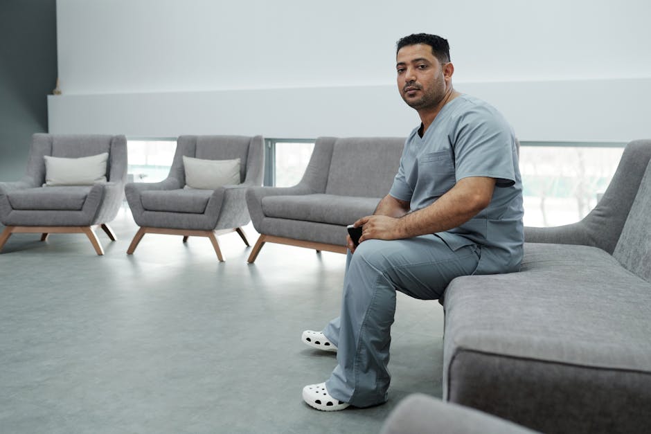Male healthcare worker in scrubs seated in a modern lounge area.