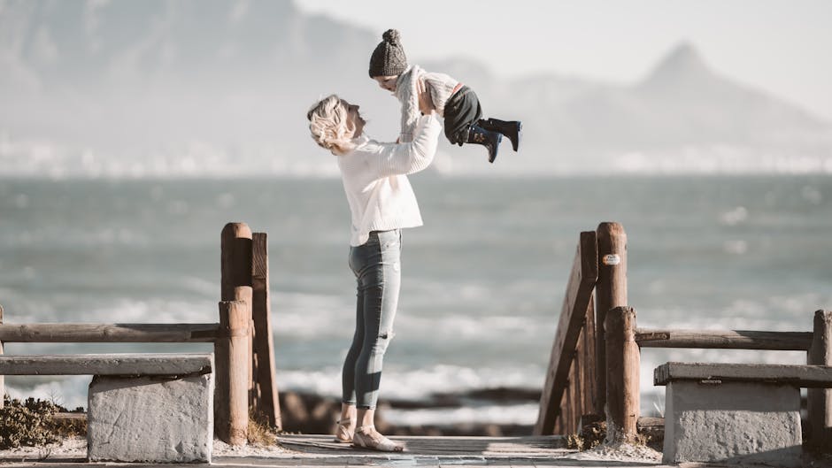 A joyful mother lifting her child near the beach on a sunny day.