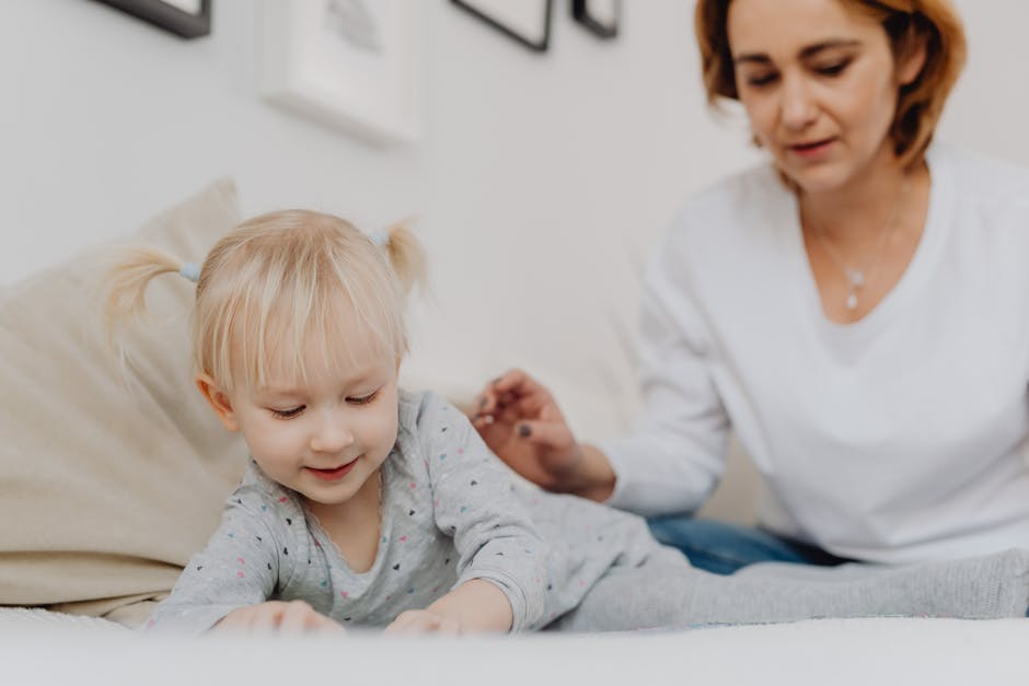 A smiling toddler with pigtails playing indoors with her mother watching.
