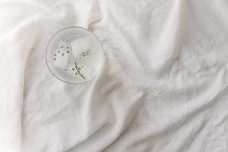 A top view of floral ice cubes in a glass on white textured fabric, showcasing minimalist elegance.