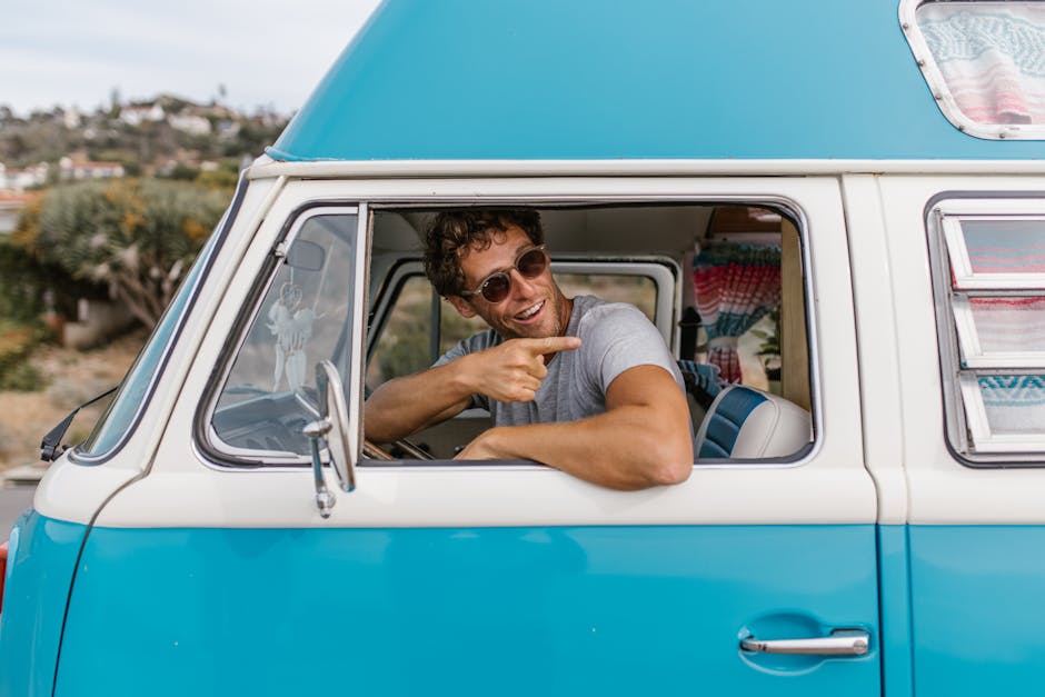 A man wearing sunglasses enjoys the summer road trip in a classic blue camper van.