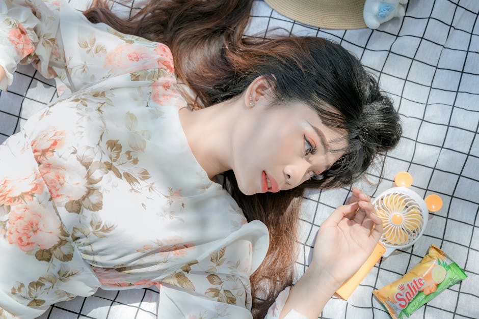 Woman in a floral dress relaxing on a grid blanket with summer essentials around her, enjoying a sunny day.