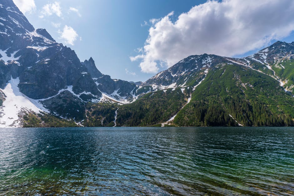 Breathtaking view of Tatra Mountains and Morskie Oko Lake with snow-capped peaks and lush greenery during spring.