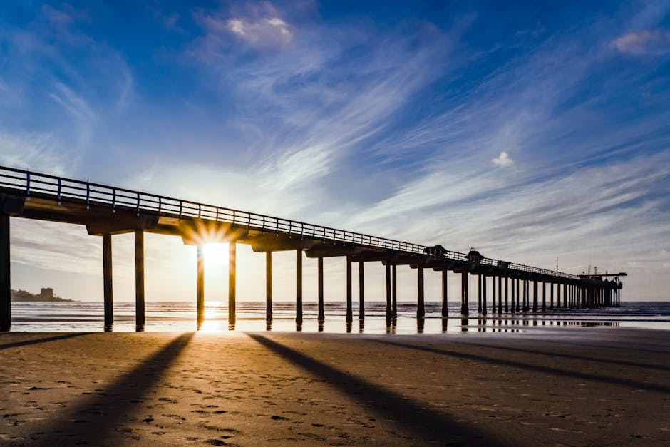 The sun rises over a picturesque pier, casting shadows on the sandy beach.