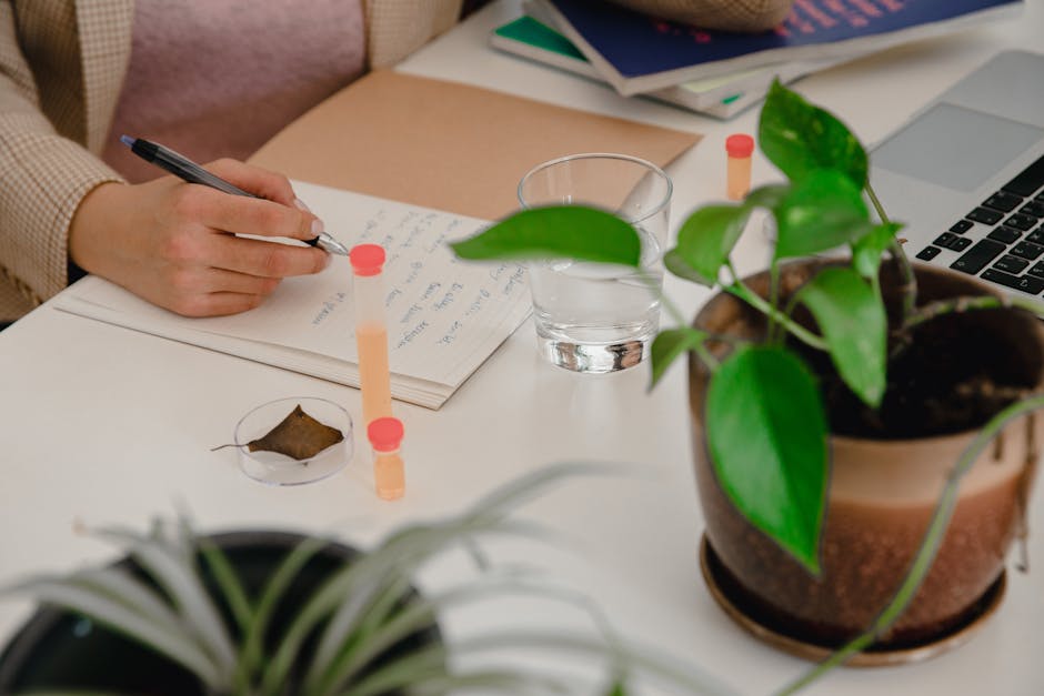A person writing in a notebook at a desk with indoor plants, creating a cozy workspace vibe.