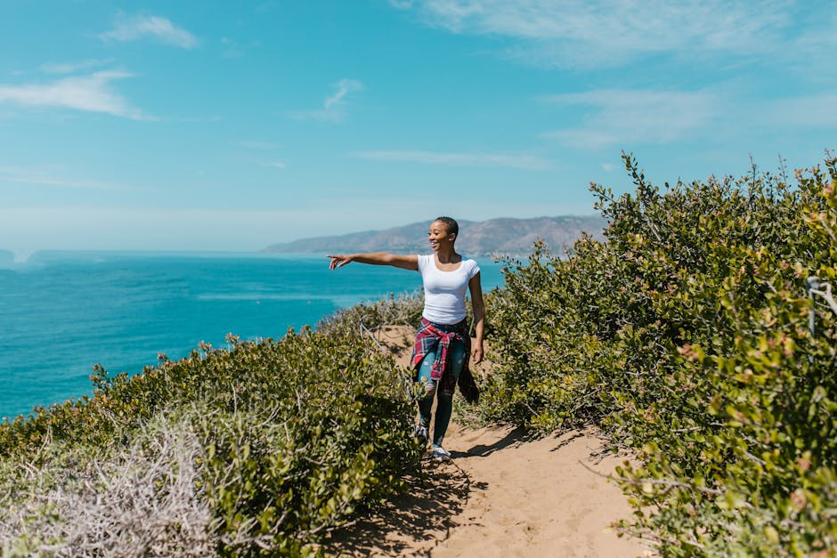 African American woman hiking a coastal trail with ocean view, pointing ahead and enjoying the outdoors.