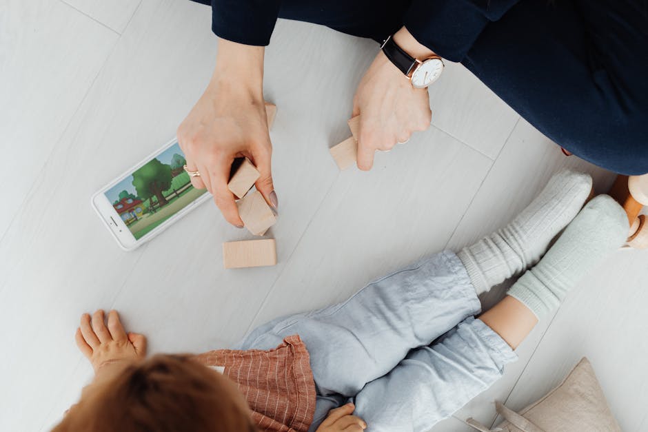 A mother and child playing with wooden blocks and a smartphone on the floor.