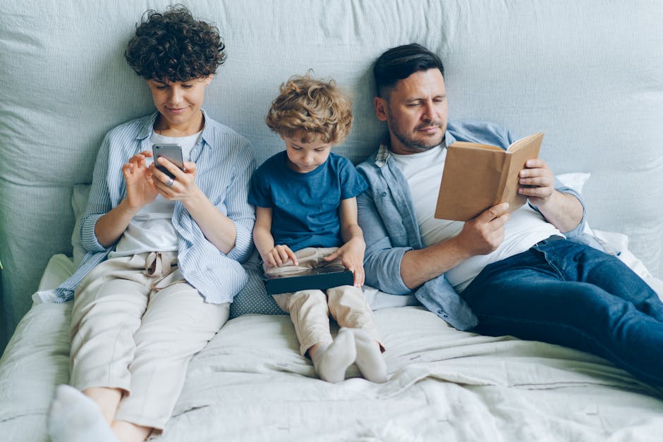 A family relaxing on bed with a smartphone, tablet, and book, symbolizing modern family life.